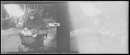 Vintage stereoscopic photo of a baby smiling in a traditional stroller outdoors, early 20th century, black and white negative.